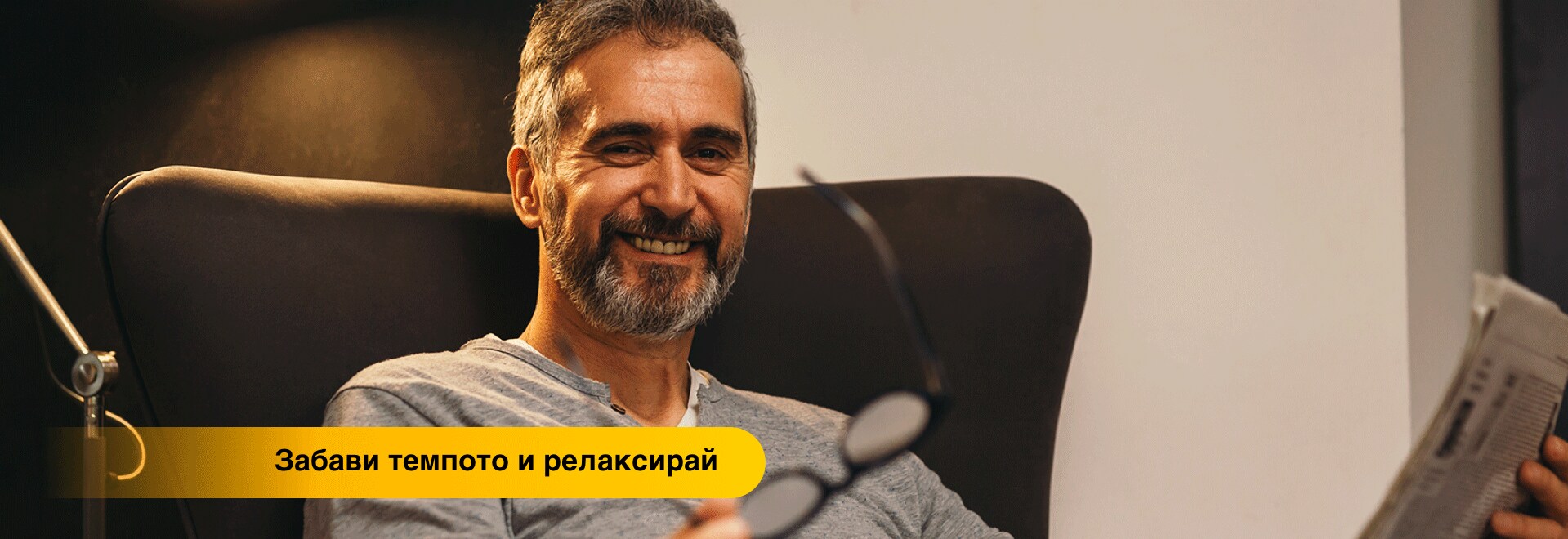 Усмихващ се мъж на средна възраст, който чете вестник.